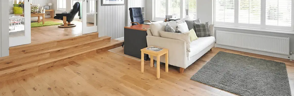 A modern living room with professionally installed laminate flooring, a beige sofa, a small side table, a gray rug, and large windows with white shutters in Fort Lauderdale, FL